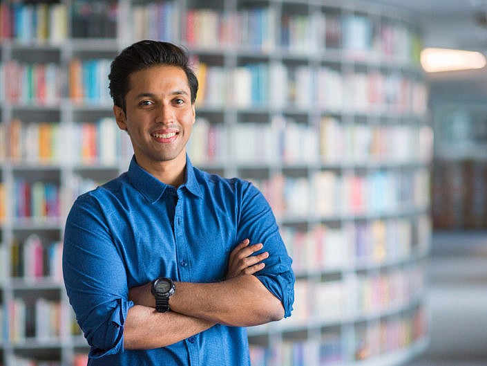 Durjoy Datta smiling in a blue shirt against a wall of books